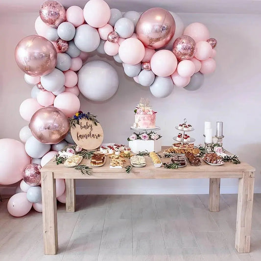 Decorative balloon arch with a baby shower setup including a cake and pastries on a table.