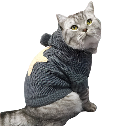 Cat wearing a gray sweater with a hood, sitting on a surface with Christmas decorations in the background.