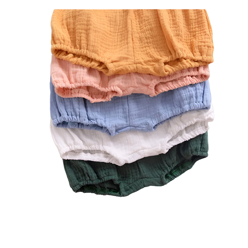 Stack of colorful baby bloomers with a leaf and paper on a white background