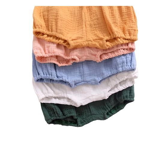 Stack of colorful baby bloomers with a leaf and paper on a white background