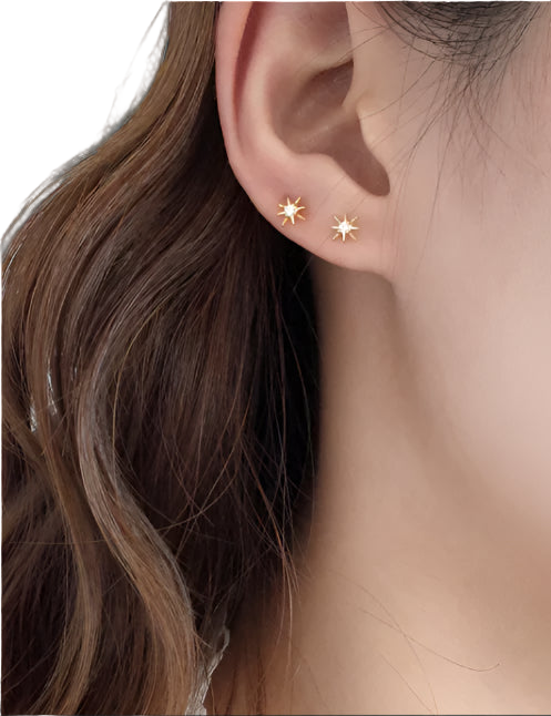 Close-up of an ear wearing gold star-shaped earrings with a neutral background