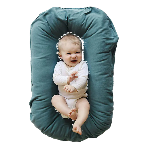 Baby lying on a green U-shaped pillow against a white background