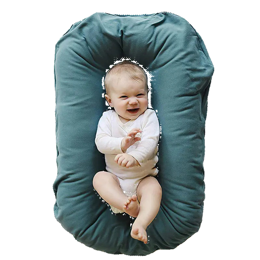 Baby lying on a green U-shaped pillow against a white background