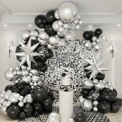 Black, silver, and white balloon arch with 'Let's Party' sign in a room with decorative wall.