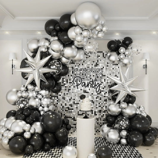 Black, silver, and white balloon arch with 'Let's Party' sign in a room with decorative wall.