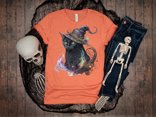 Orange t-shirt with a black cat in a witch's hat design, surrounded by Halloween-themed items on a wooden surface.