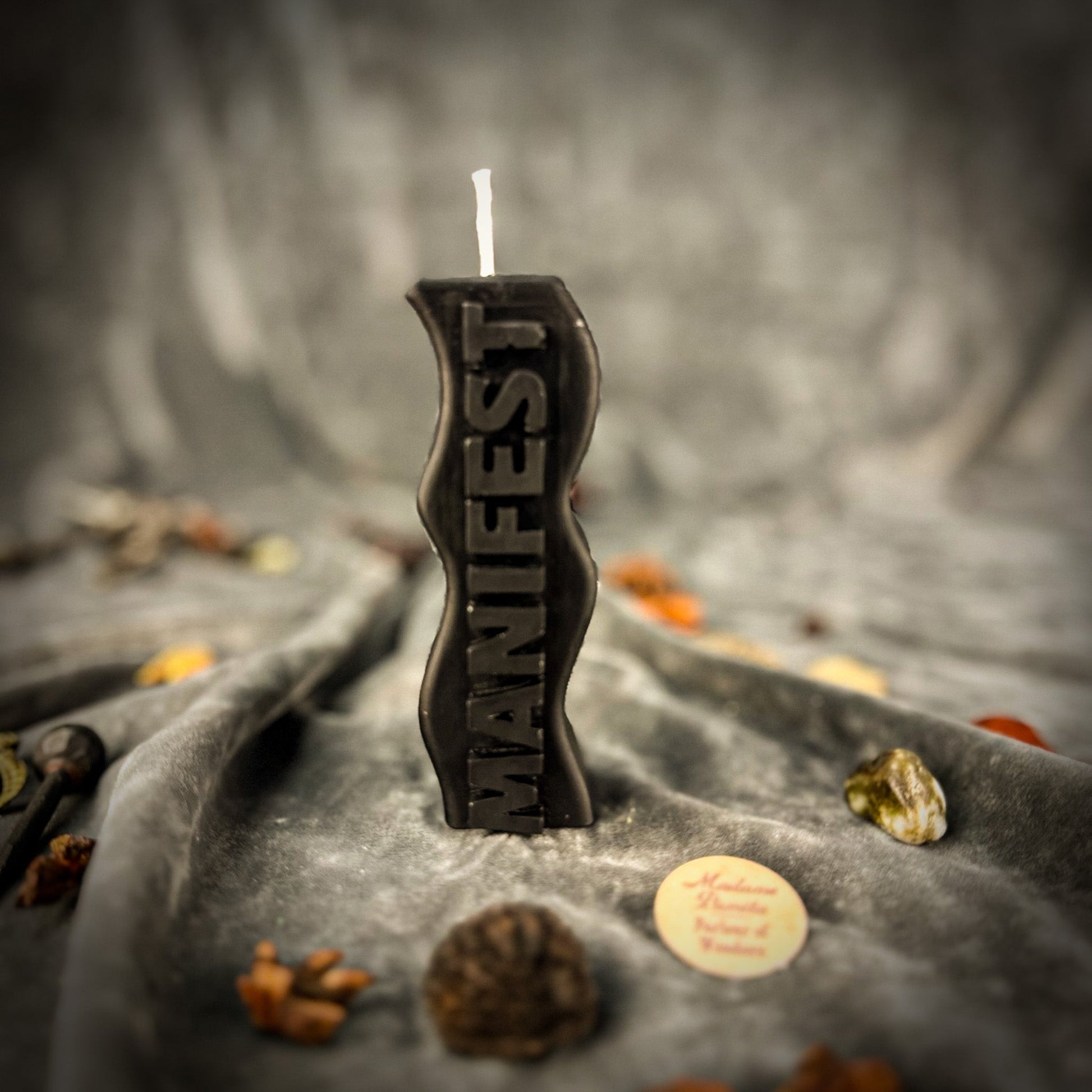 Black candle with 'Witch' text on a dark, textured surface with autumn leaves.