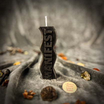 Black candle with 'Witch' text on a dark, textured surface with autumn leaves.