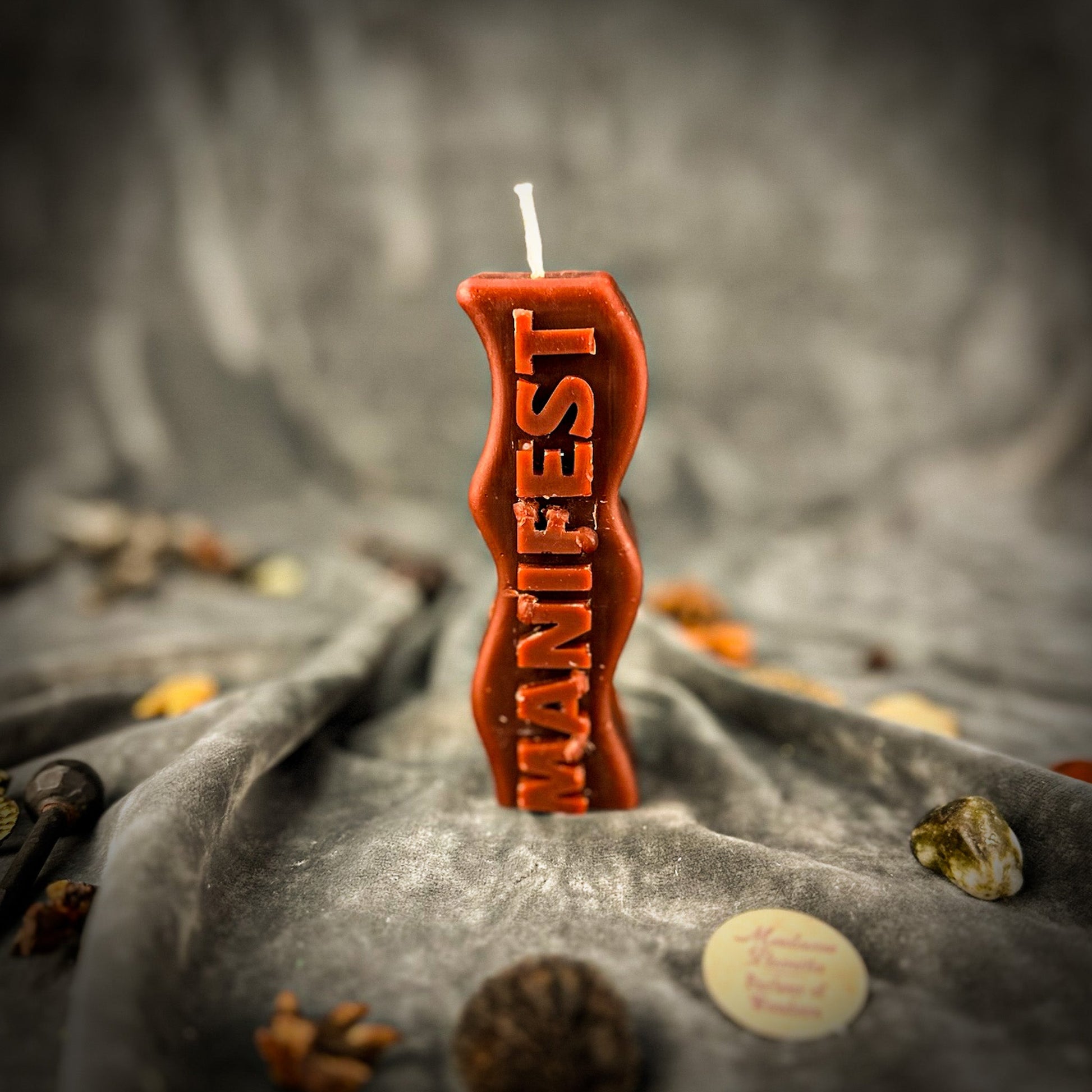 Candle with 'MANIFEST' text on a textured surface