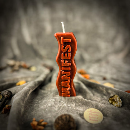 Candle with 'MANIFEST' text on a textured surface