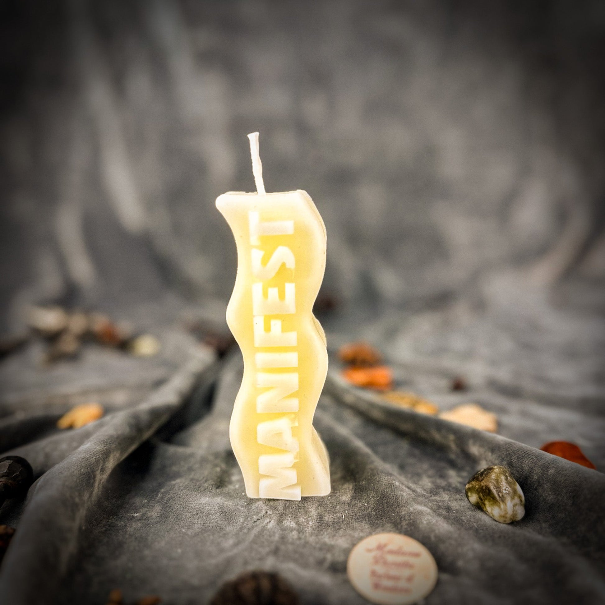 Candle with 'MANIFEST' text on a textured surface with stones and crystals.