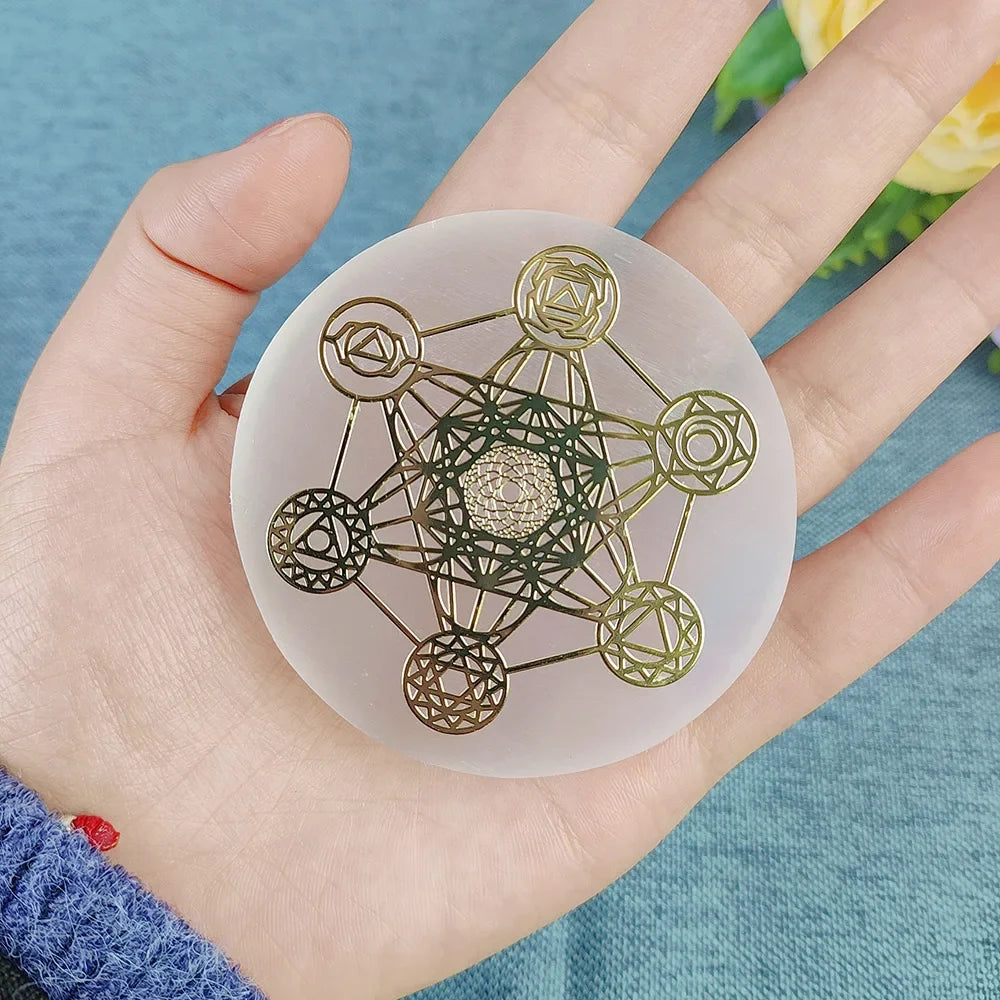 Hand holding a round, transparent object with intricate gold and green designs against a blue background.