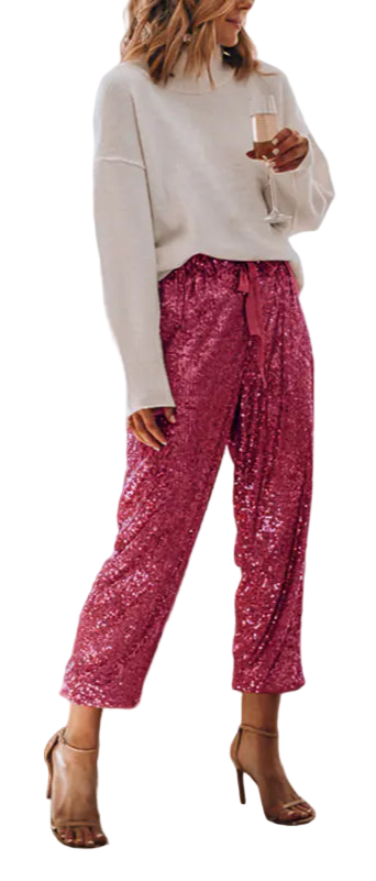 Woman in pink sequin pants and white sweater standing in a living room with a Christmas tree.