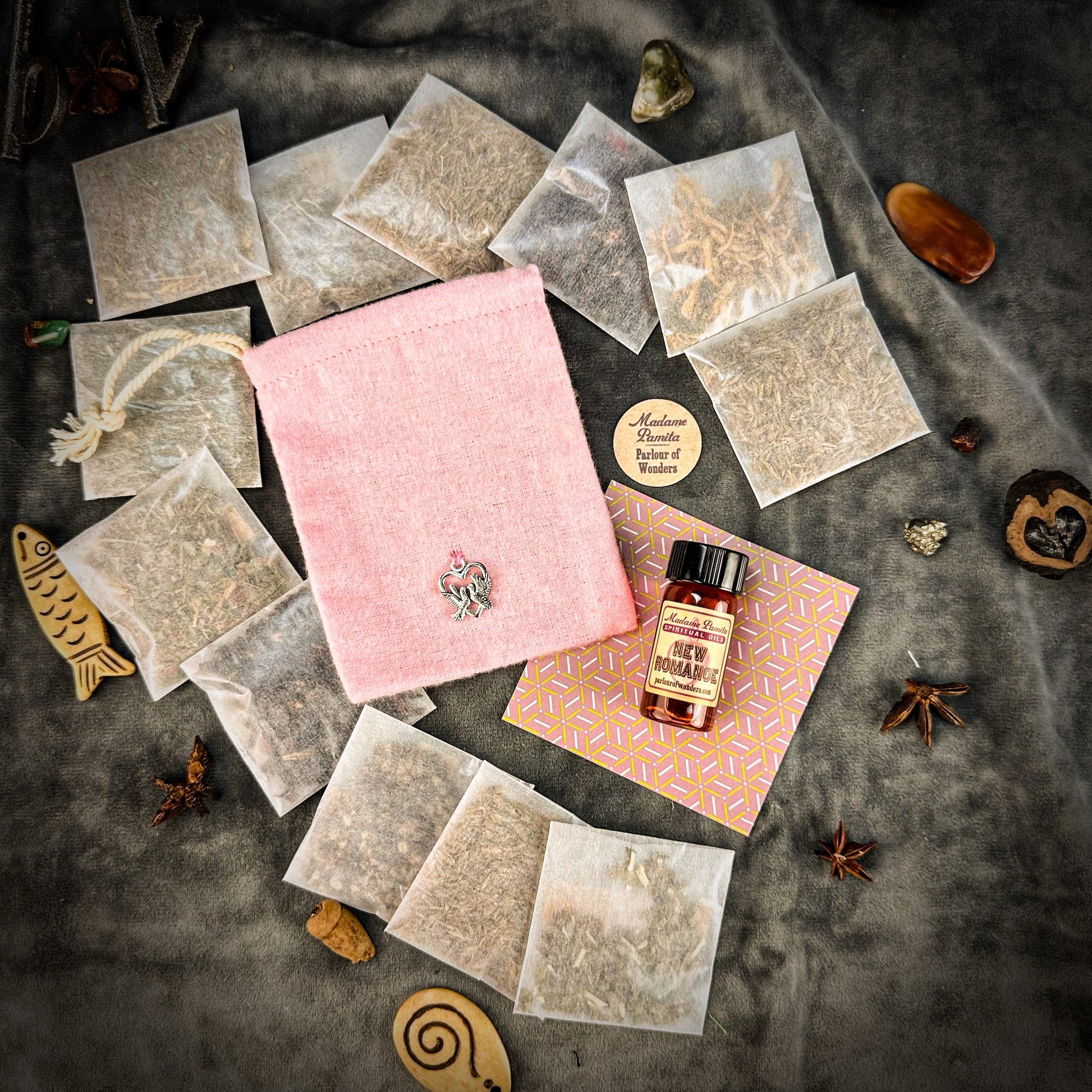 Tea bags, pink velvet pouch, and a bottle on a textured surface with decorative elements.