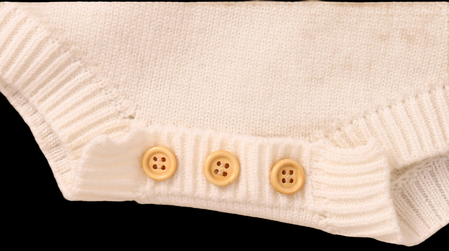 Close-up of a white knitted garment with three buttons on a wooden surface