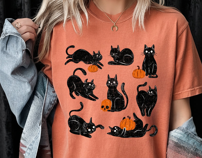 Person wearing an orange t-shirt with black cat and pumpkin designs.