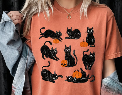 Person wearing an orange t-shirt with black cat and pumpkin designs.