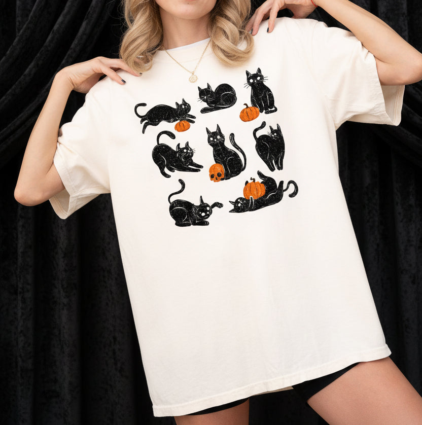 Person wearing a white t-shirt with black cat and pumpkin designs on a plain background