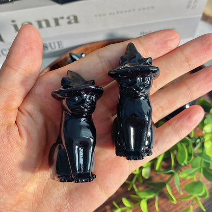 Two black cat figurines held in a hand with a blurred background