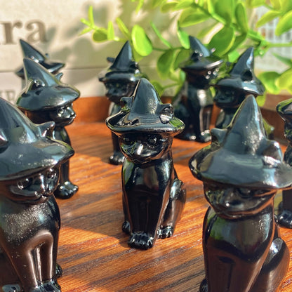 Black cat figurines wearing witch hats on a wooden surface with greenery in the background