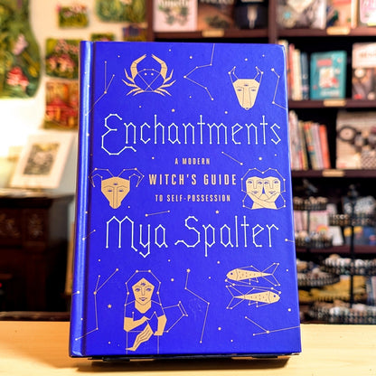 Blue book titled 'Enchantments' by Mya Spalter on a shelf with books and decor in the background