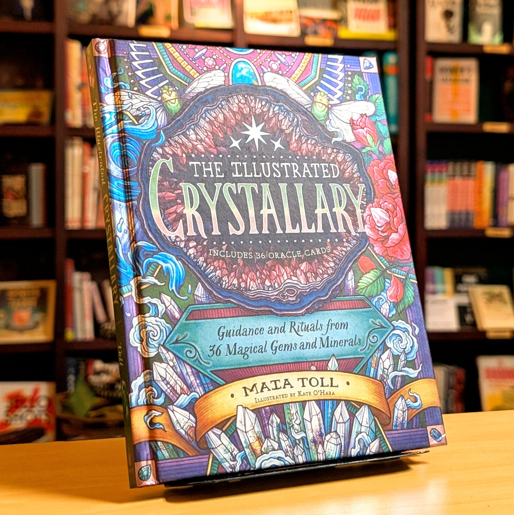 Colorful book titled 'The Illustrated Crystallary' on a wooden surface with a bookshelf background.