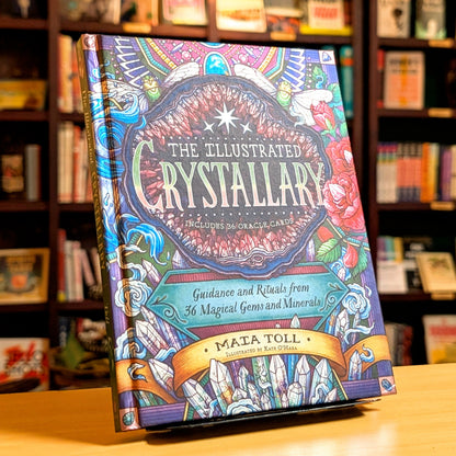 Colorful book titled 'The Illustrated Crystallary' on a wooden surface with a bookshelf background.