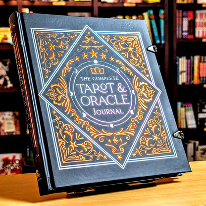 The Complete Tarot & Oracle Journal standing upright on a wooden table with a blurred bookshelf background.