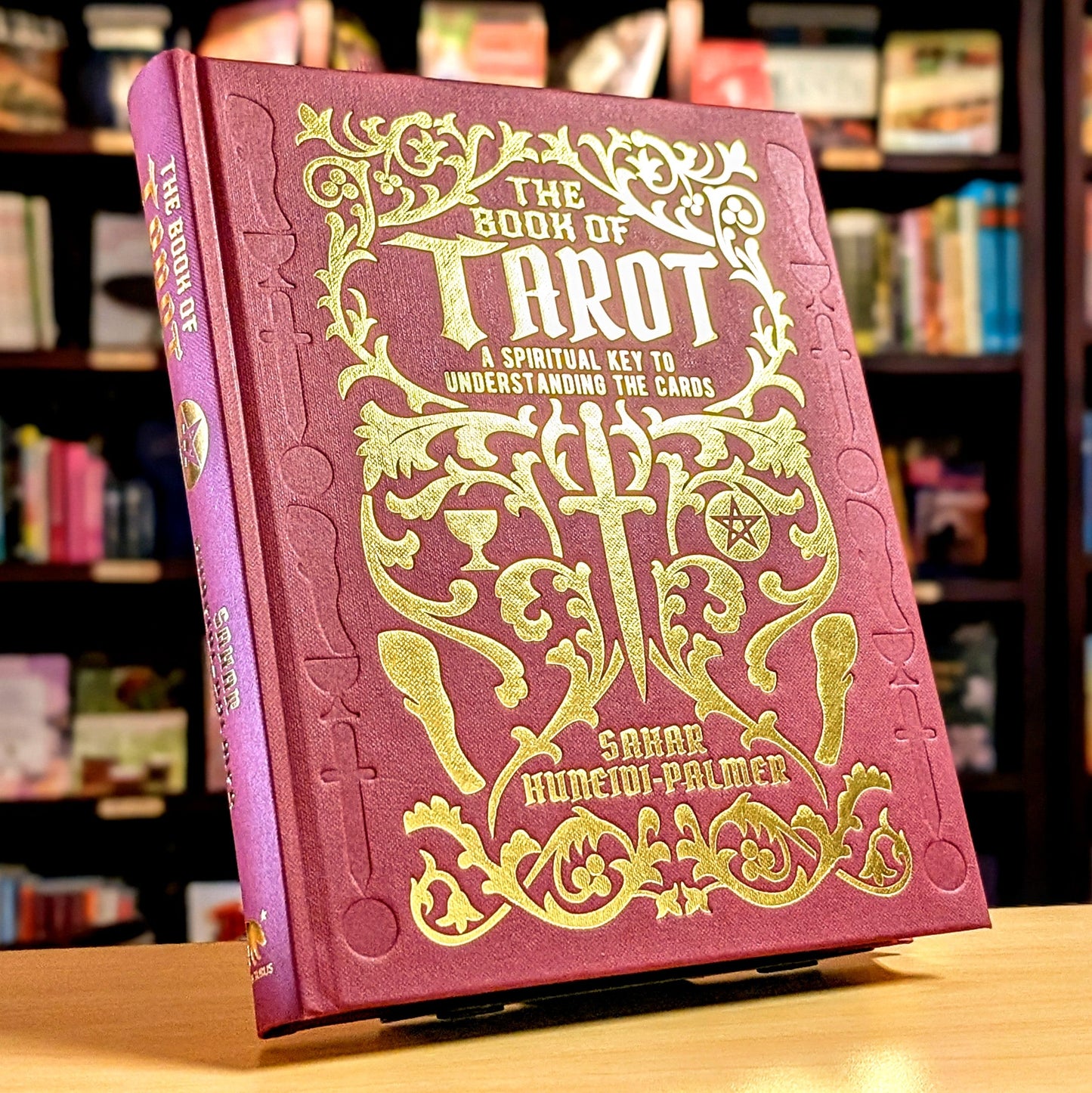 Book of Tarot with gold embossed text on a wooden surface with blurred bookshelf background