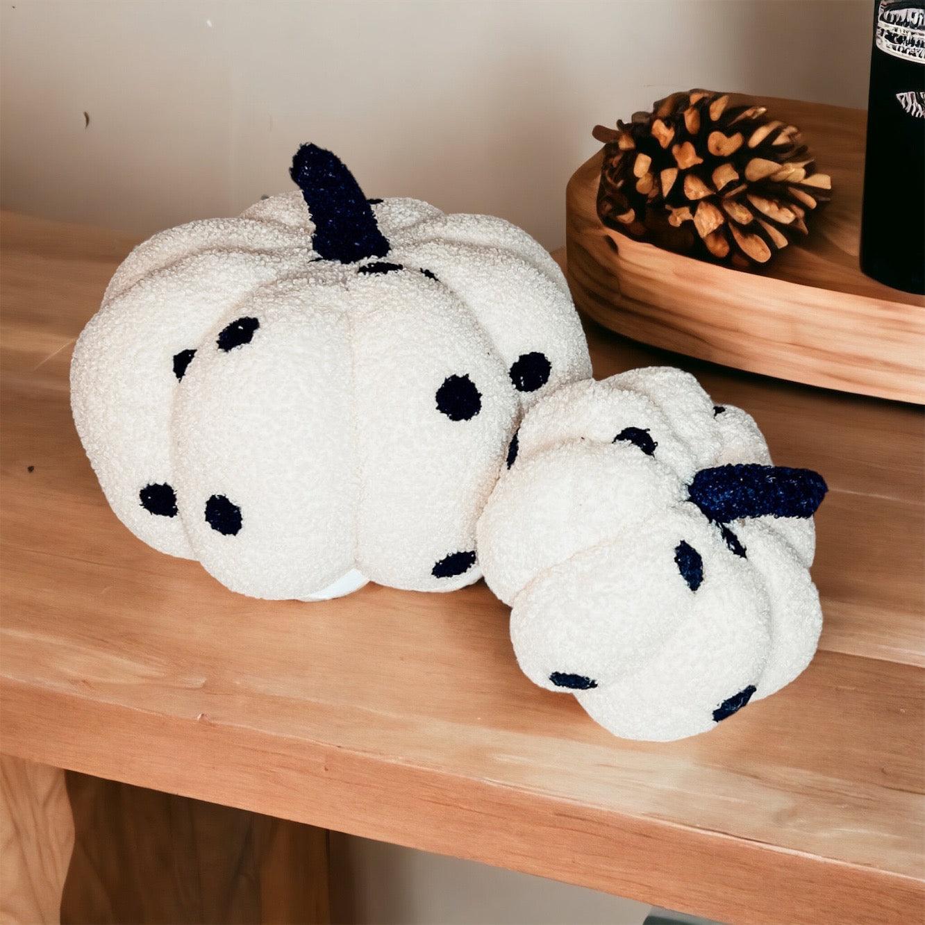 Two white plush pumpkins with black spots on a wooden surface.