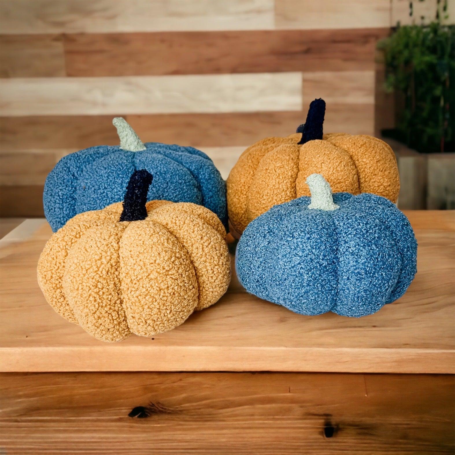 Three textured pumpkins in blue and orange on a wooden surface with a wooden wall background.