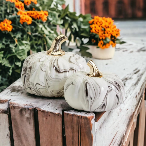 Marble-patterned pumpkins with gold stems on a wooden surface with flowers in the background