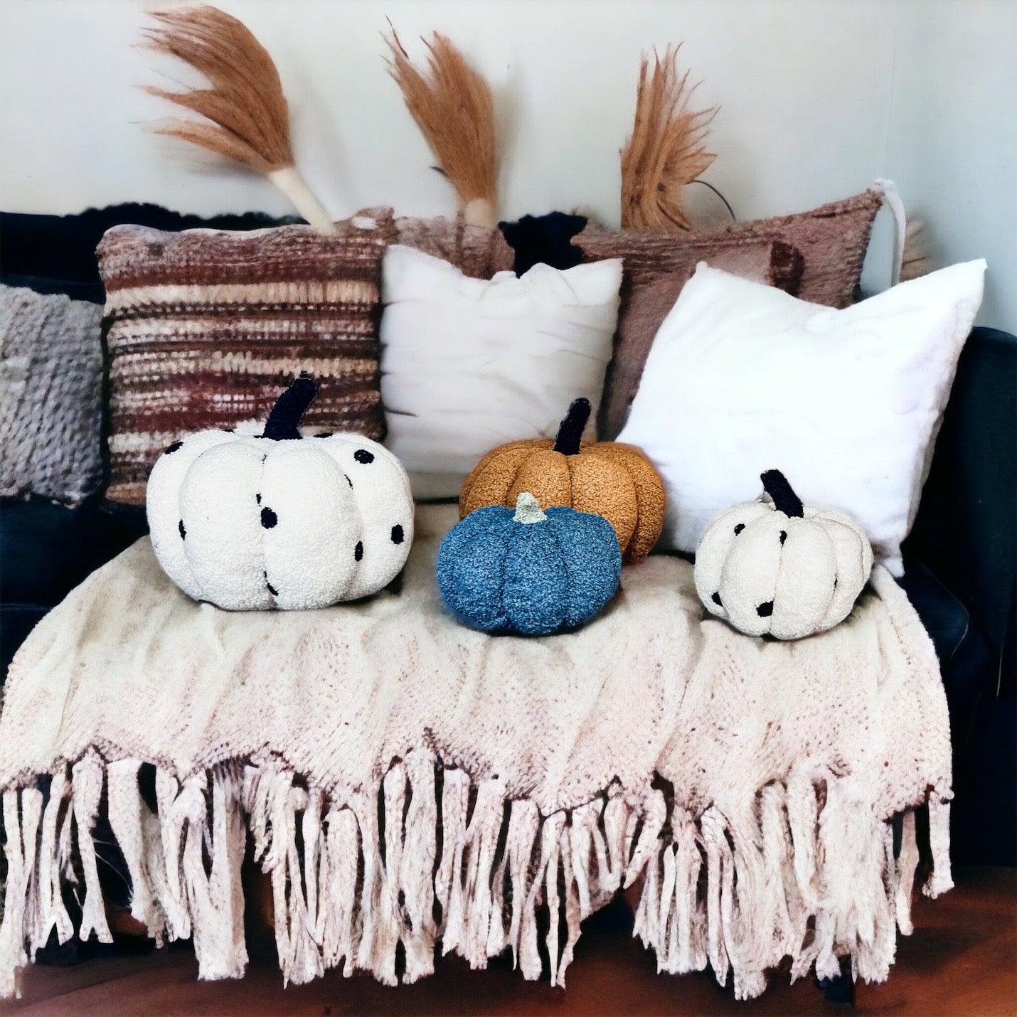 Decorative pumpkins on a blanket with pillows and dried plants in the background