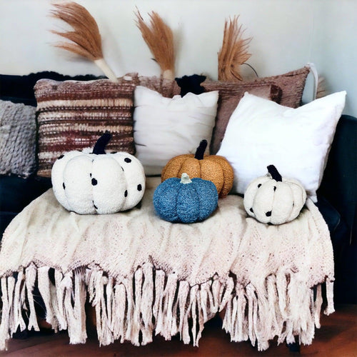 Decorative pumpkins on a blanket with pillows and dried plants in the background