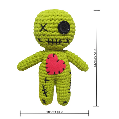 Green crochet doll with a black button eye and red heart on a white background