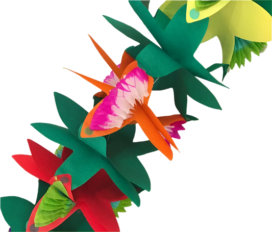 Colorful paper flowers on a white surface with green leaves in the background