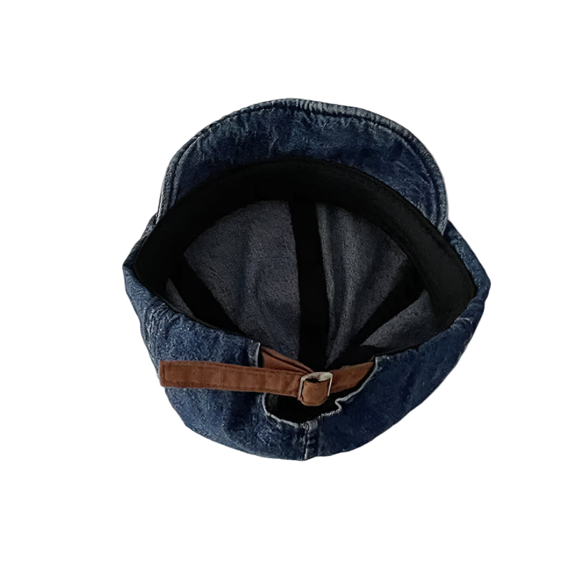 Blue denim cap with a brown leather strap on a light beige background