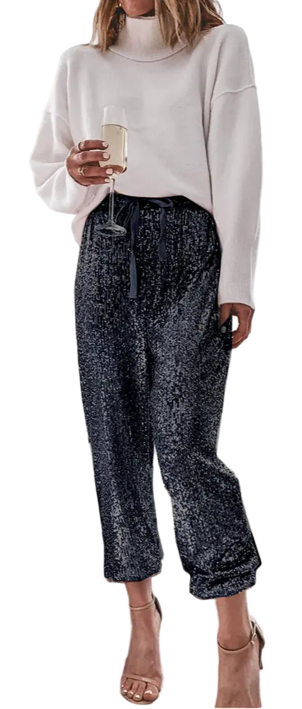 Woman in a living room holding a glass of wine, wearing a white sweater and patterned pants.
