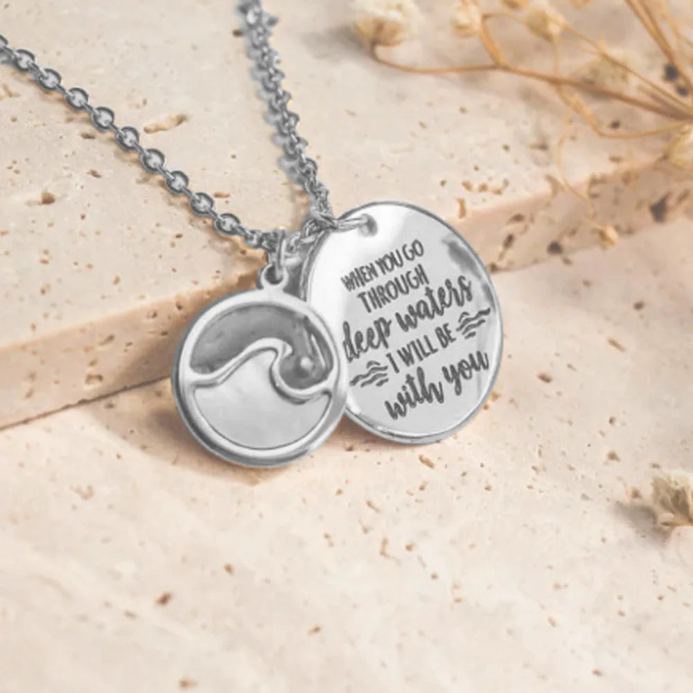 Silver necklace with wave design and engraved message on a beige background