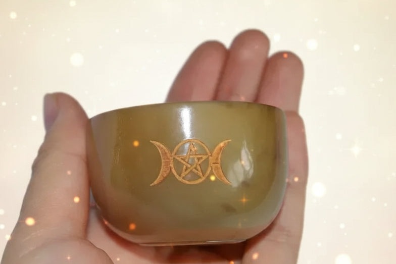 Hand holding a small brown bowl with a gold symbol on a white background