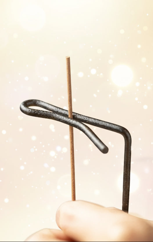 Hand holding a thin metal rod with a black coil on a dark background