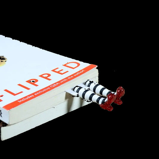 Book titled 'Flipped' with a decorative figure on top, next to wireless earbuds on a wooden surface.