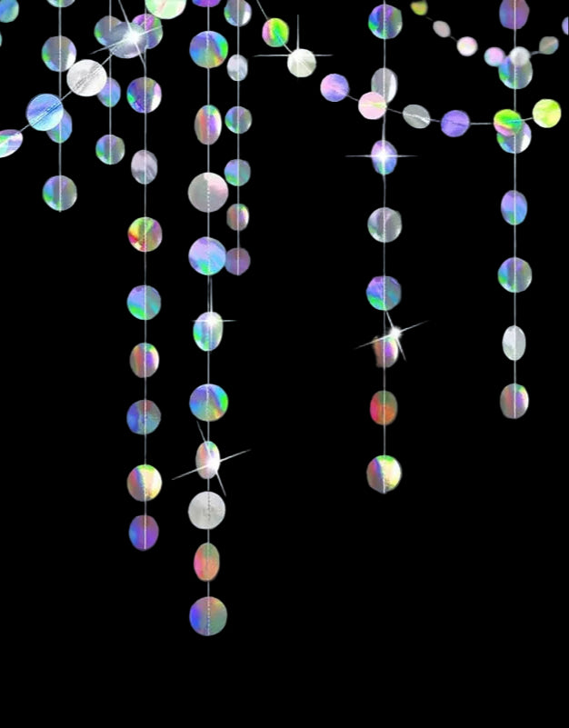 Iridescent string lights hanging against a dark wall with two lit candles on a surface below.