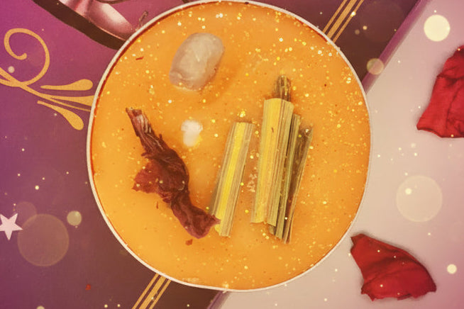 Decorative setup with a round orange dish containing items, red rose petals, and a purple book with gold accents.