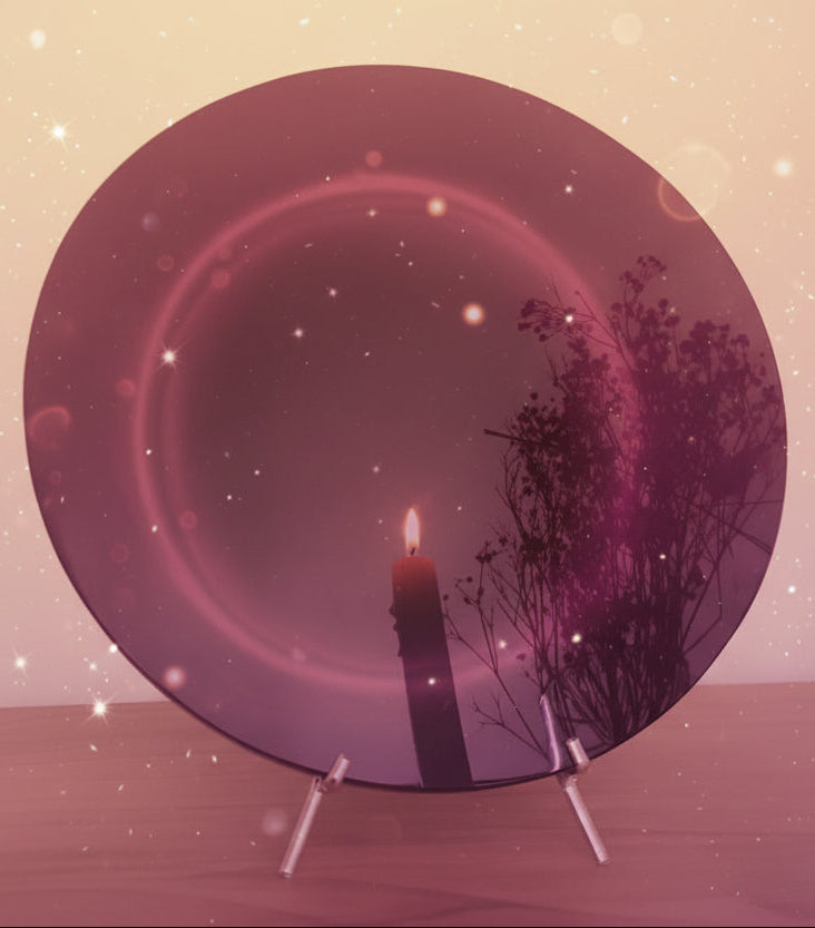 Round mirror reflecting a candle and branches on a wooden surface