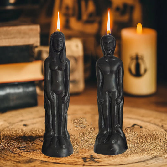 Two black statue-shaped candles with lit wicks on a wooden surface.