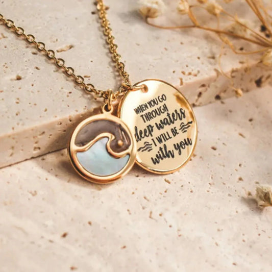 Gold necklace with wave pendant and engraved message on a beige background
