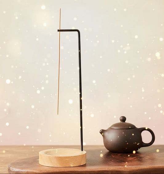 Incense stick holder on a wooden surface with a teapot in the background