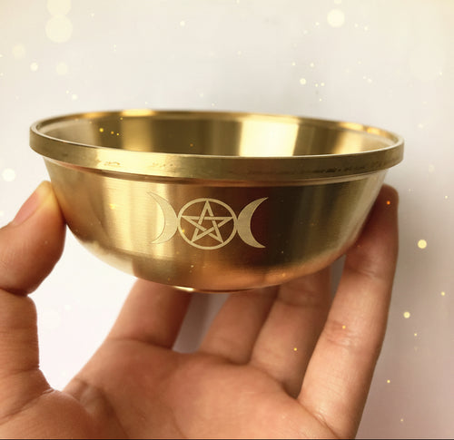 Gold bowl with engraved symbols held by a hand against a white background