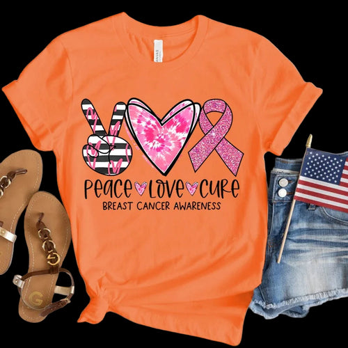 Orange t-shirt with peace, love, cure breast cancer awareness design on a wooden surface.